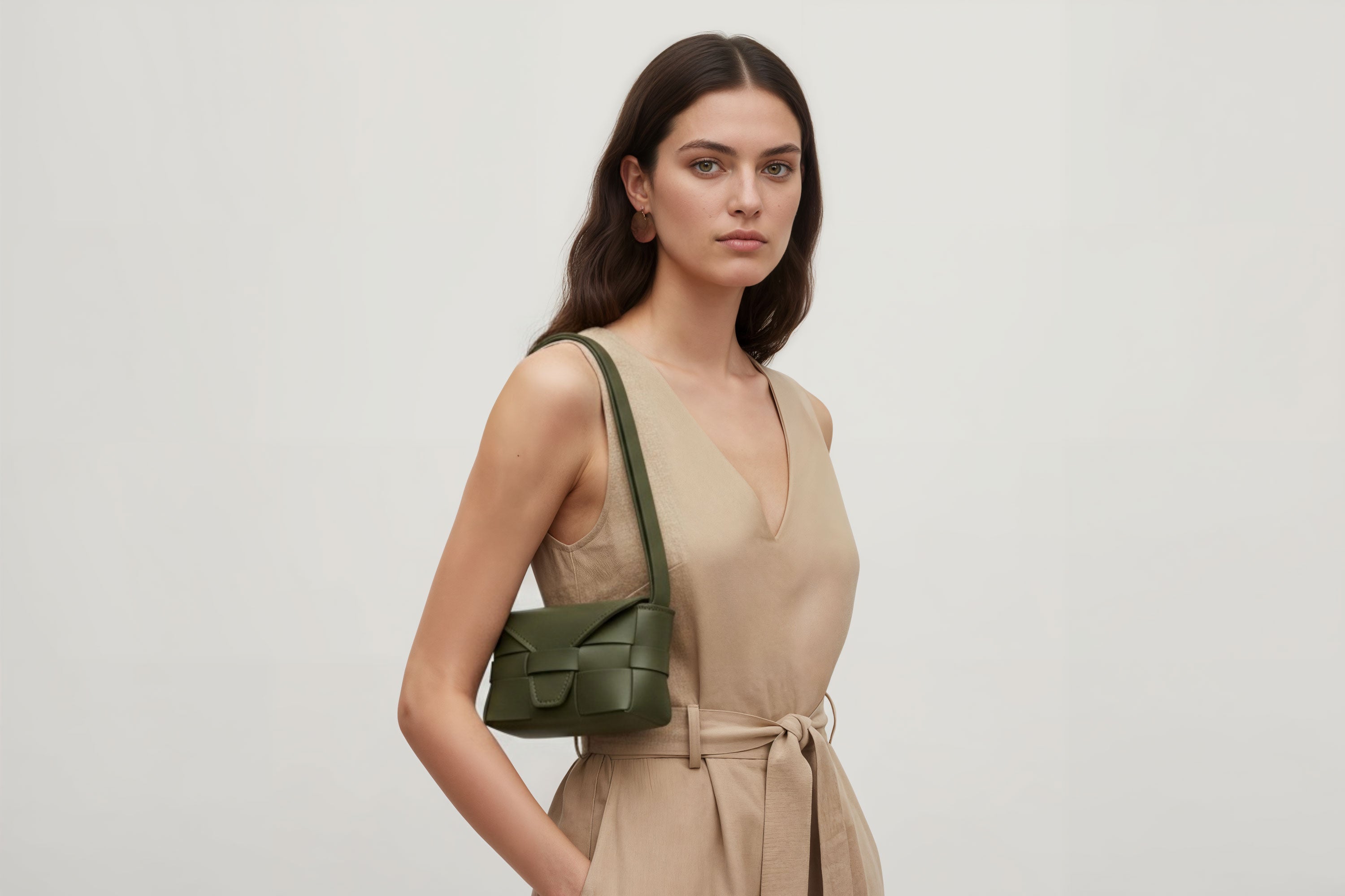 Woman wearing the olive green small Saka leather bag against a plain background. Minimalist design from Atelier Madre - Manuel Dreesmann in Barcelona