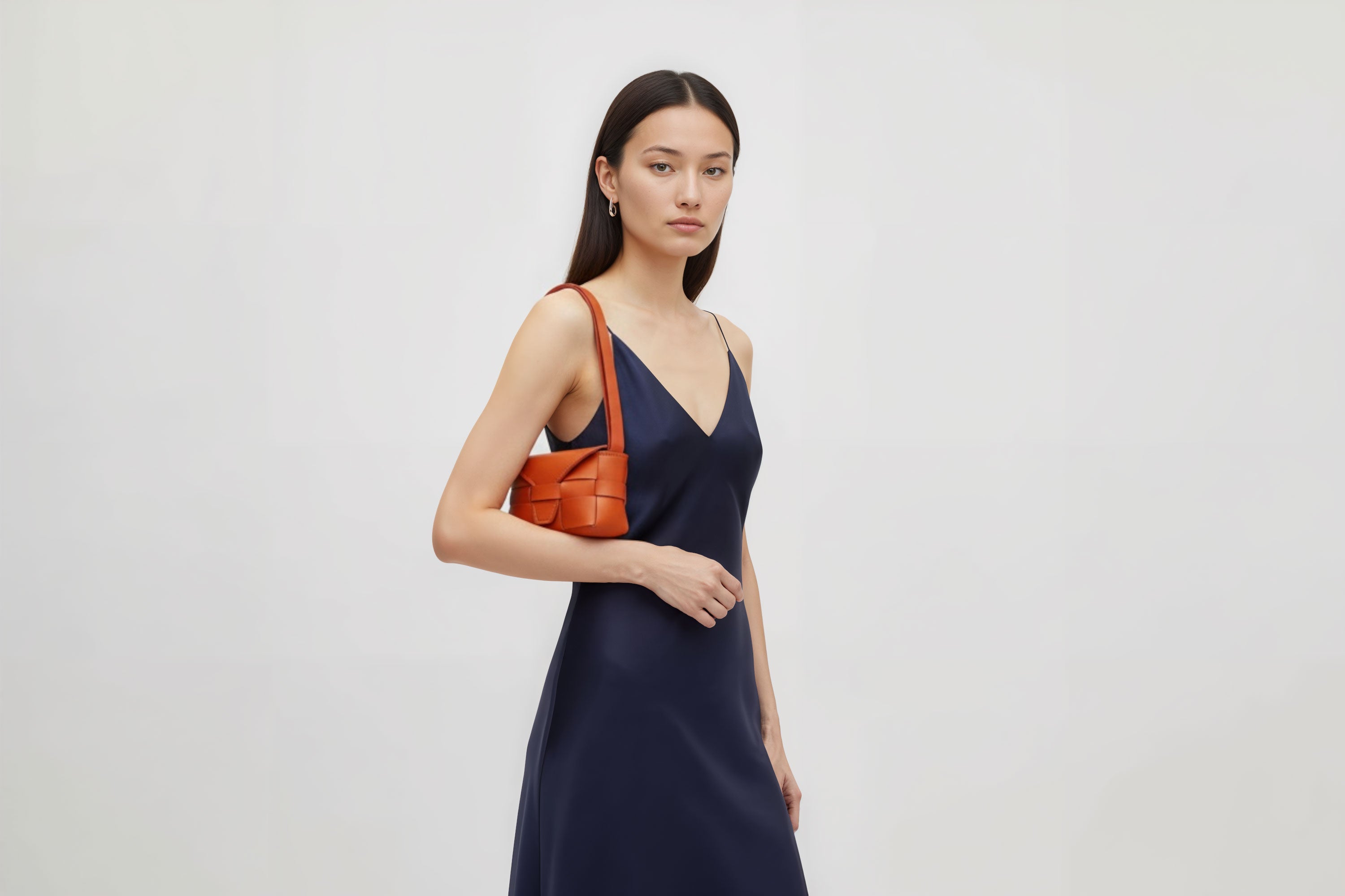 Woman wearing the orange color small Saka leather bag against a plain background. Minimalist design from Atelier Madre - Manuel Dreesmann in Barcelona