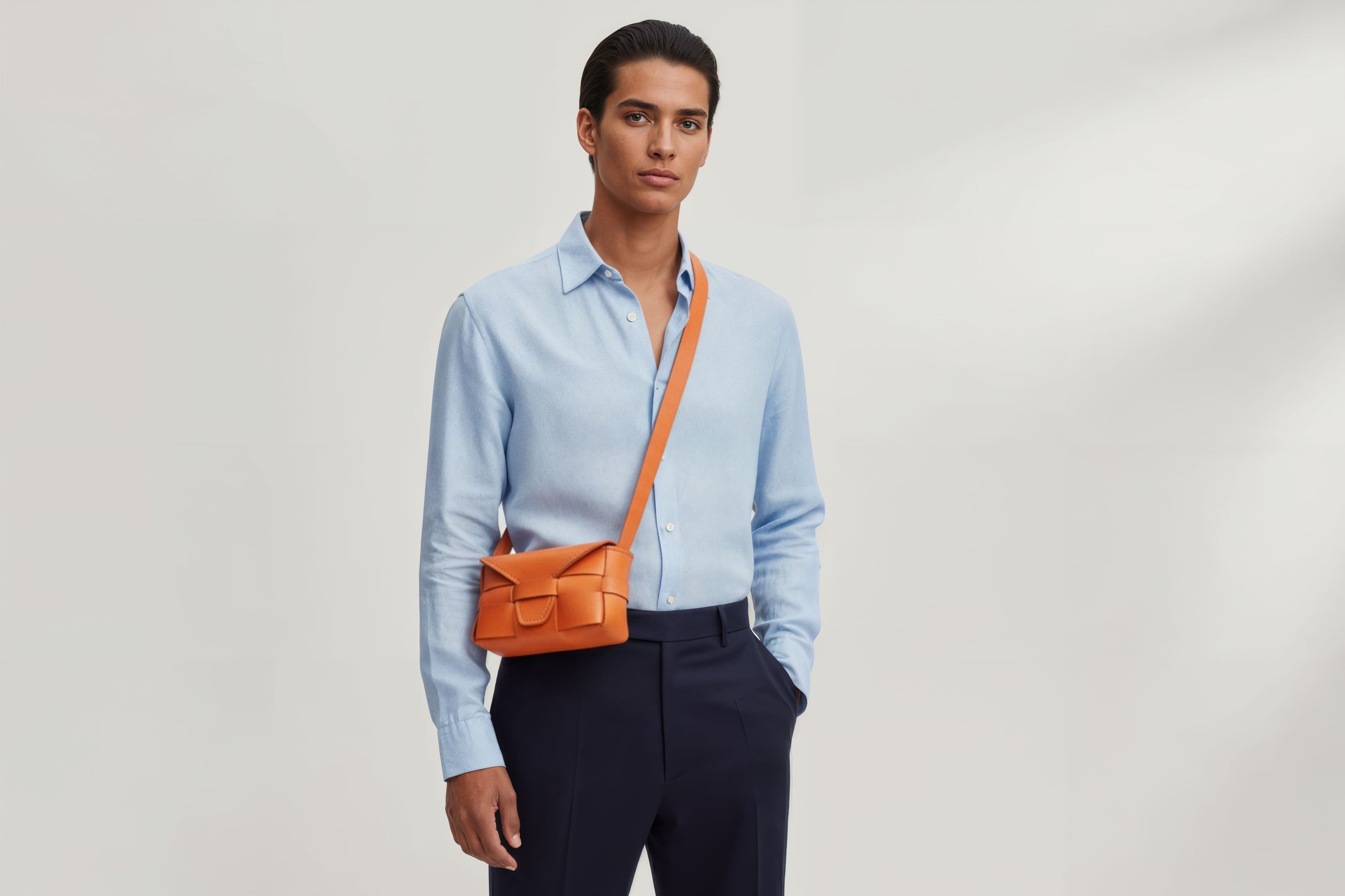Man wearing the orange color small Saka leather bag against a plain background. Minimalist design from Atelier Madre - Manuel Dreesmann in Barcelona