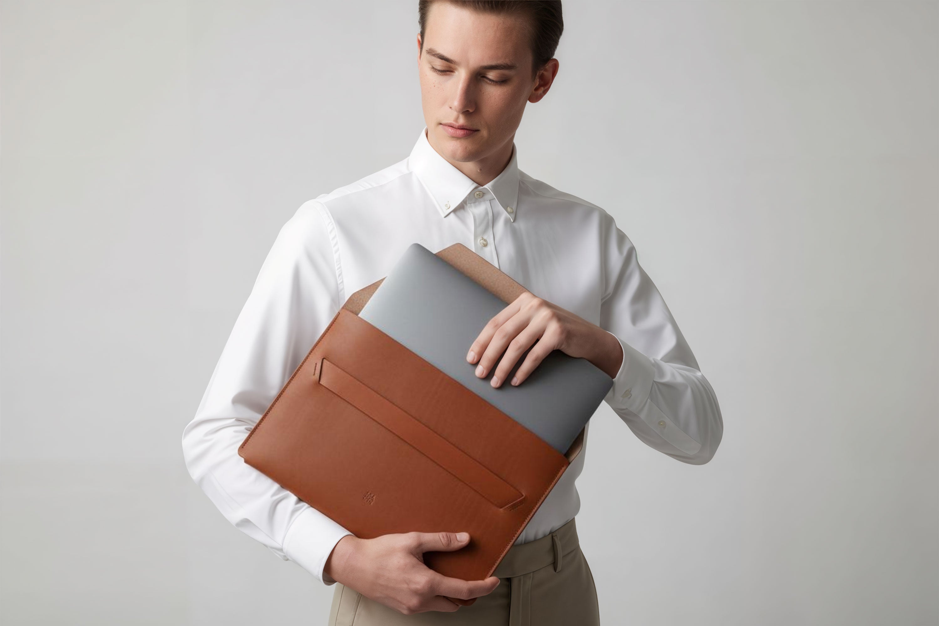 Man holding a leather sleeve for a MacBook in dark brown color in front of bright background minimalistic design atelier Madre Manuel Dreesmann Barcelona Spain