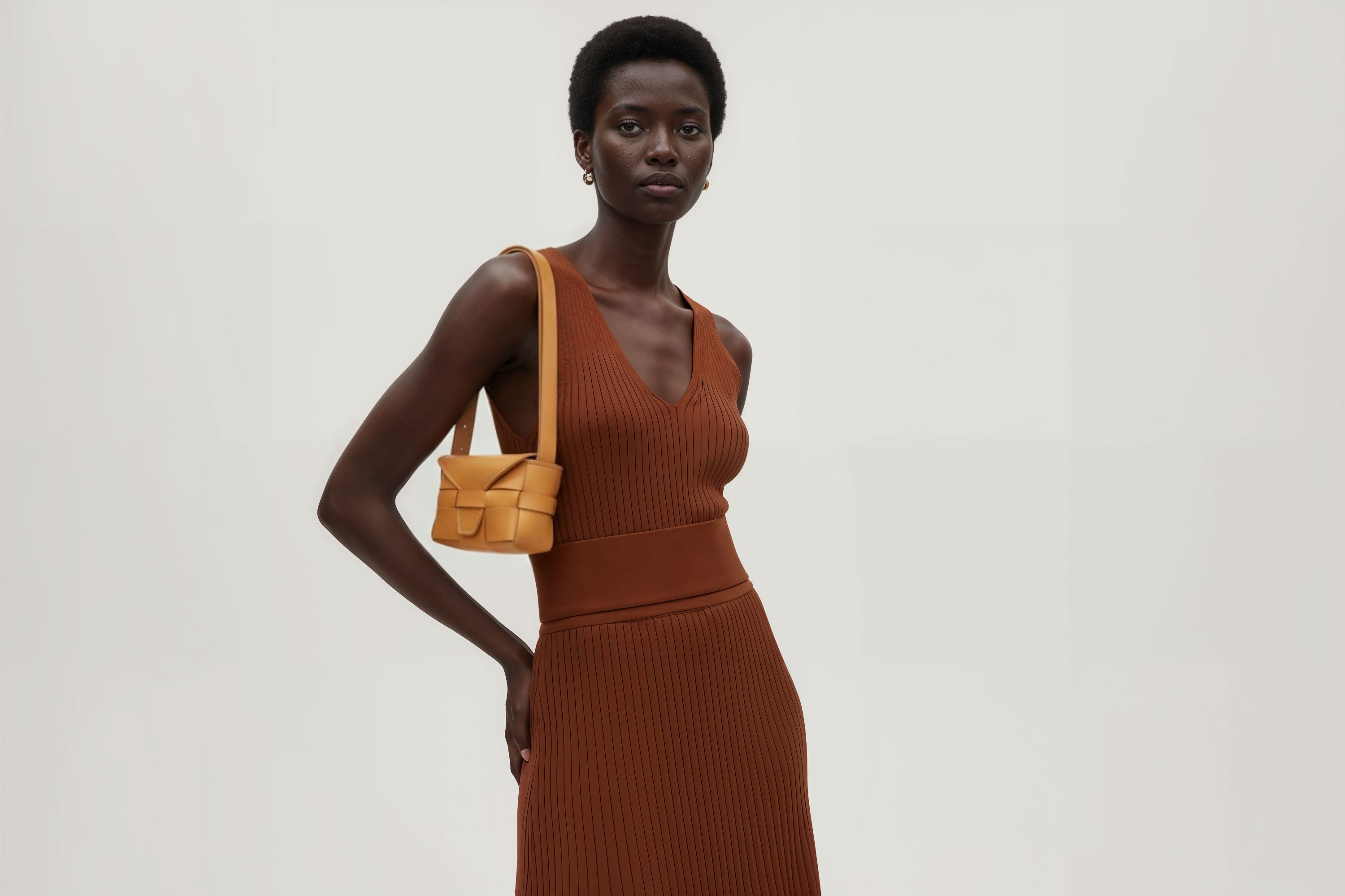 Woman wearing the brown small saka leather bag against a plain background. Minimalist design from Atelier Madre - Manuel Dreesmann in Barcelona